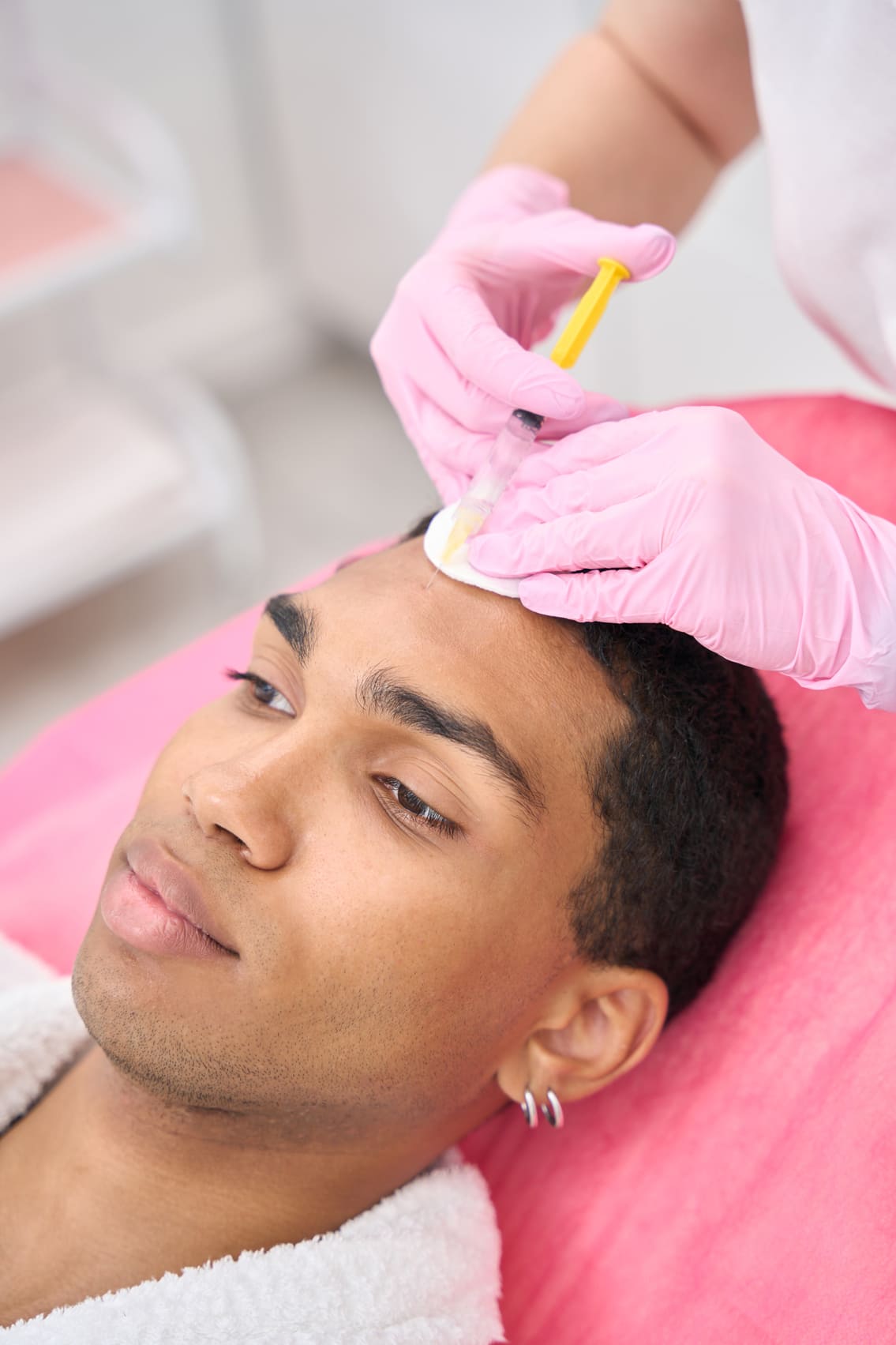 Profesional aplicando un tratamiento de cuidado de la piel en el rostro de un hombre joven.