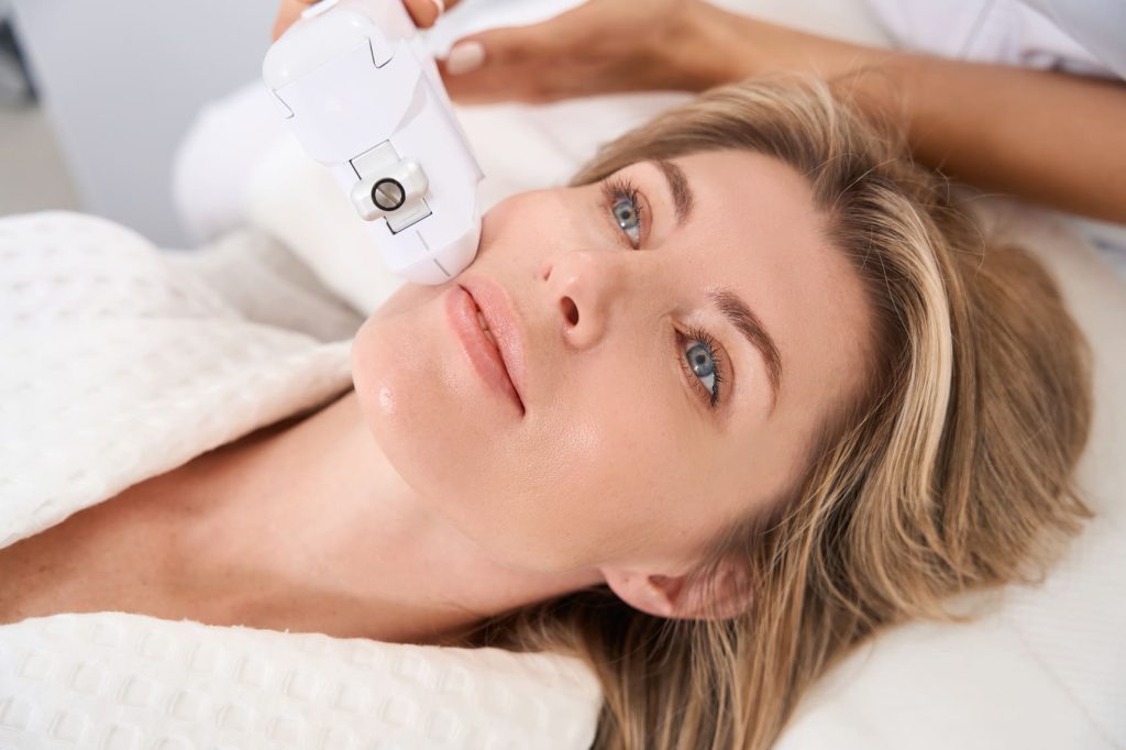 Mujer recibiendo un tratamiento facial con un dispositivo de tecnología avanzada.